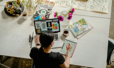 photo of woman writing on tablet computer while using laptop